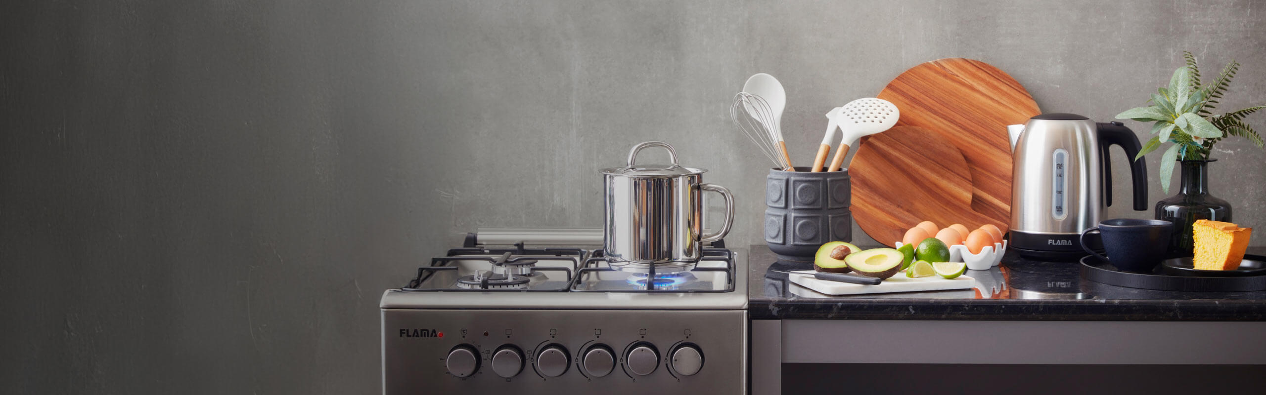 Chaleira elétrica (ou jarro elétrico) de inox da Flama numa bancada de cozinha ao lado de uma fatia de bolo e chávena