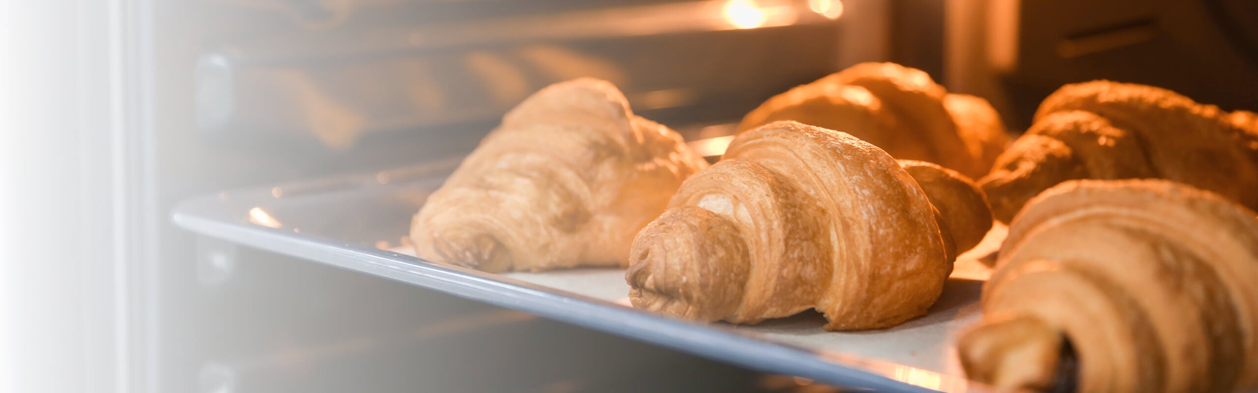 Croissants dourados a cozer num tabuleiro dentro de um mini forno elétrico da marca Flama